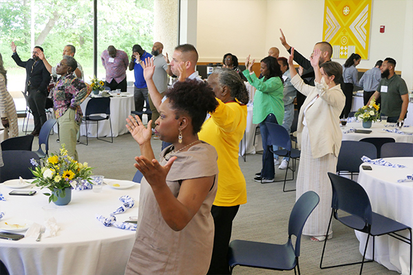 A group of people lift their hands in respect during a worship service.