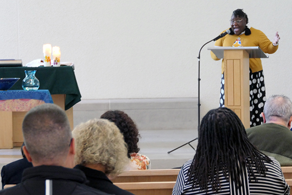 A woman stands at a pulpit in front of an audience in a chapel.